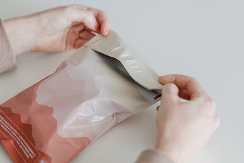 Hands opening a sealed impack.co SALE - Mountain Clay Mailer, 10" x 13", against a plain background, designed for medium-sized shipments to ensure optimal transit protection.