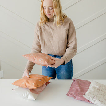 A woman is putting mailer bags 10" x 13" from impack.co on a table.