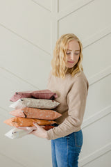 A person in casual attire holds a stack of impack.co's Wildflower Biodegradable Mailers, measuring 10" x 13", against a patterned wall, exuding rustic charm.