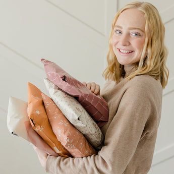A girl holding a stack of mailer bags 10" x 13" from impack.co in front of a white wall.