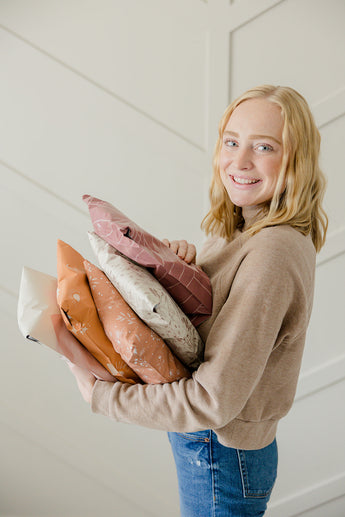 A girl holding a stack of biodegradable mailer bags 10" x 13" from impack.co in front of a white wall.