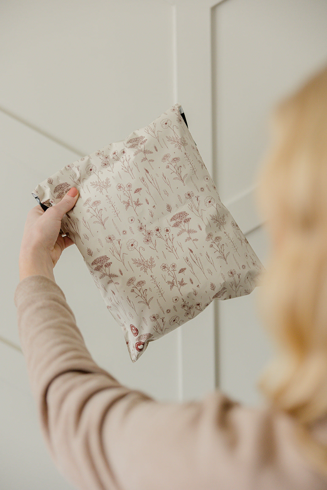 A person holding a white impack.co biodegradable mailer with a wildflowers print in the size of 6" x 9".