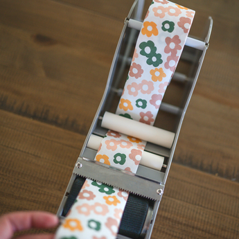 Impack.co's SALE - Packing Tape - Daisy Multi glides effortlessly over wood surfaces, revealing a lively floral pattern. Perfect for eco-friendly packaging, this water-activated gummed tape imbues every wrap with a natural charm.
